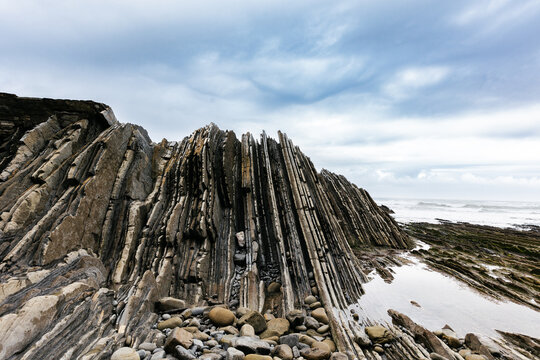 Rocky flysch formations near sea under gloomy cloudy sky