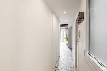Horizontal shot of a long bright corridor with an entrance door and a view of the living room with...