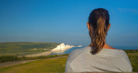CLOSE UP, DOF: Back view of young tourist admiring stunning Seven Sisters cliffs