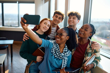 Group of happy college friends taking selfie with cell phone in classroom.