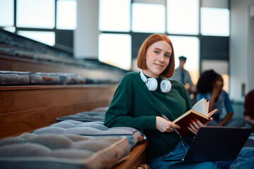 Smiling female student learning in lecture hall and looking at camera.