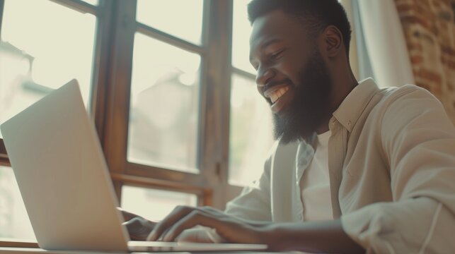 Smiling Bearded African Man Using Laptop At Home While Sitting The Wooden Table, Male Hands Typing On The Notebook Keyboard, Concept Of Young People Work Mobile Devices