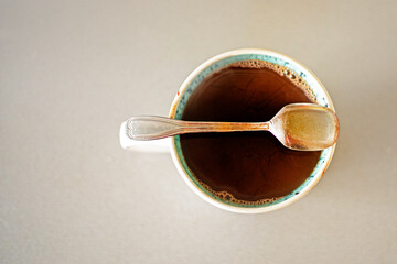 cup with hot natural chocolate and a teaspoon on a gray table, top view. snack