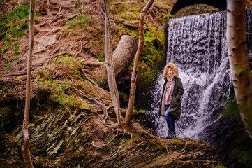 Young Woman Contemplating Nature by a Waterfall Under a Stone Arch Bridge