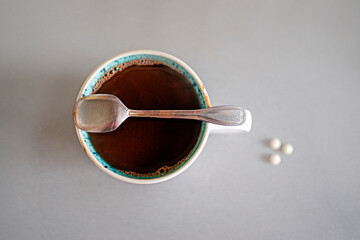 cup with hot natural chocolate and a teaspoon on a gray table and dietary supplements, top view....