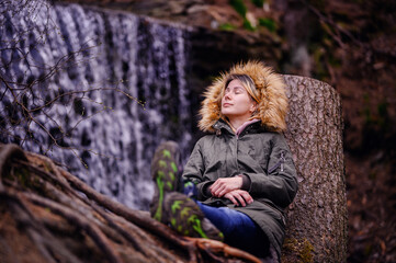 Person Relaxing Against a Tree Trunk Near a Waterfall in a Forest