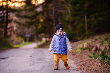 Fototapeta premium Child Walking Alone on a Country Road Surrounded by Forest at Dusk