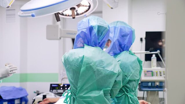 Two doctors wearing robes and protective helmets stand near the operational table. Surgeons preparing for the surgery.