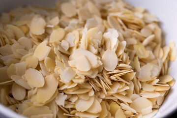 A tasty food portrait of a white bowl full of almond flakes used by a baker to create tasty cookies or pastries. The chopped up crunchy cooking and baking ingredient is ready to be used.