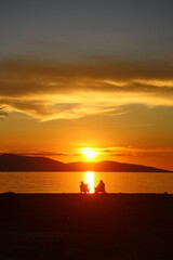 Fototapeta premium two people talking by the sea at sunset and a lonely fishing boat in the sea