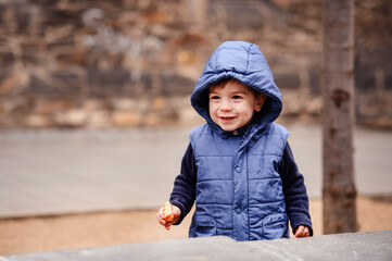 Cheerful Toddler in Blue Hooded Jacket Holding a Cookie on a Stone Ledge