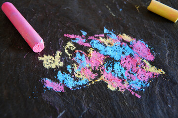 Pastel colored chalk mix of blue, yellow and pink on a dark textured stone surface