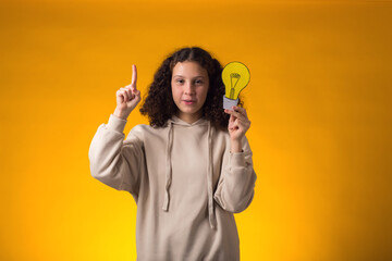 Surprised girl holding paper bulb and pointing finger up. Success, motivation, winner, genius, idea concept