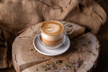 A transparent glass cappuccino cup stands on a stump