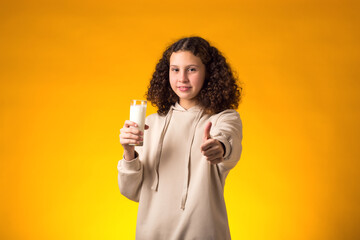Smiling girl holding glass of milk and showing thumb up gesture. Nutrition and health concept