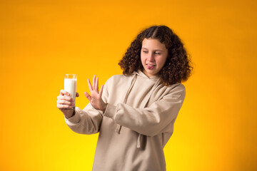 Girl with dairy allergy holding glass of milk on yellow background. Lactose intolerance concept