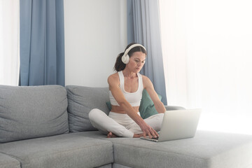 woman sitting cross legged on the sofa and using her laptop and headphones