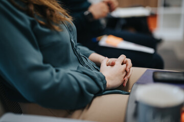 A selective focus shot capturing a female professional with clasped hands during a consultative or educational setting. Evokes themes of anxiety, anticipation, or focus.