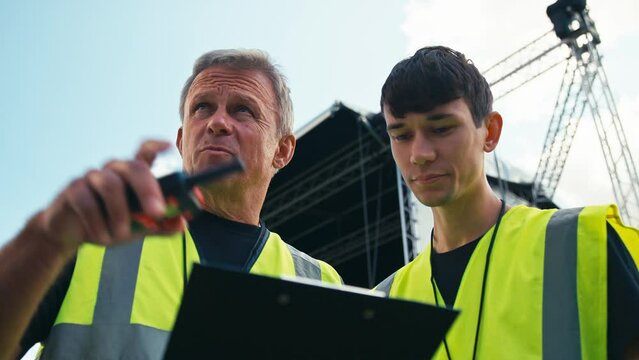 Male Production Team With Clipboard Setting Up Outdoor Stage For Music Festival 