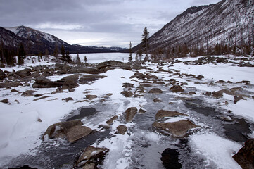 Natural landscape of a frozen river and lake surrounded by snowy mountains.
