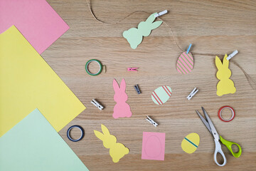 Paper crafts. Creating an Easter garland with bunnies and eggs for school, classroom, home, children's room. Colored cardboard, rabbits and eggs cut out of paper, decorative clothespins, scissors.