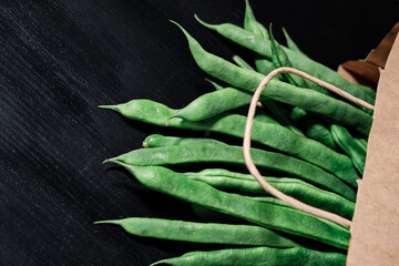raw fresh string green beans in organic paper bag on black wooden background