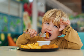 happy boy with blond hair eats fries and nuggets in restaurant