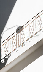 A sunlit staircase on Paros Island casts intricate shadows against a whitewashed wall. The ornate iron railing adds a touch of elegance to this minimalist, Mediterranean scene.