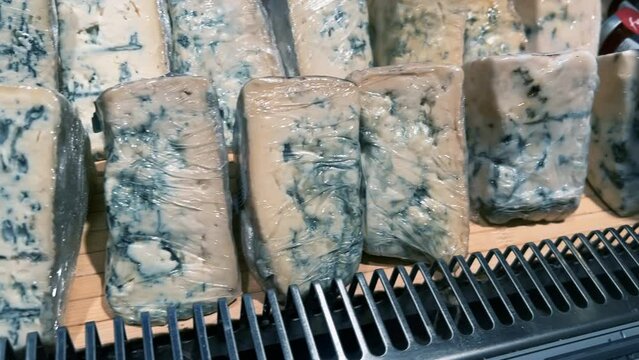 Blue mold cheese cut into slices lies on the display of an open refrigerator in a supermarket or grocery store