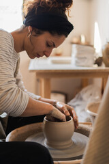 An artisan potter focused on shaping a smooth clay pot on the pottery wheel, demonstrating the art of ceramic making