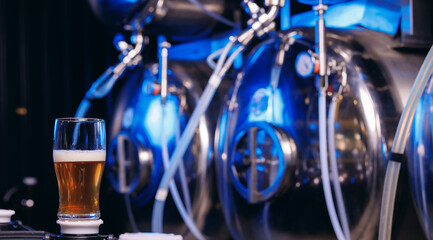 Commercial equipment for bottling drink for bar. Glass of beer against background of steel tanks at...