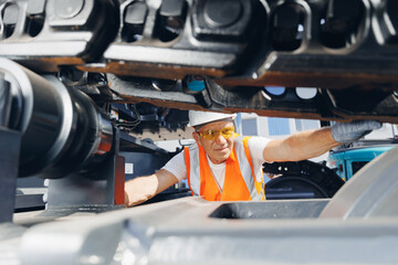 Man in hard hat, industrial worker mechanic checks hydraulic hose system equipment on excavator