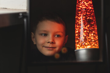 7 years old boy in the darkness looking at a soft red light of a lava lamp