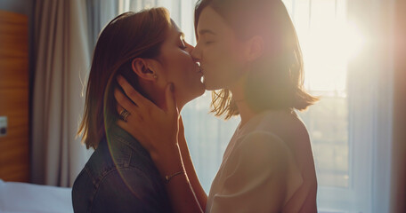 Lifestyle portrait of young lesbian couple on romantic vacation embracing and kissing in hotel bedroom, intimate moment, in love