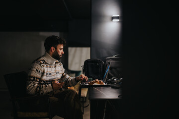 Focused man using laptop in dimly lit room: Remote work after hours.