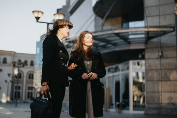 Confident businesswoman in elegant attire walking with colleague in urban setting.