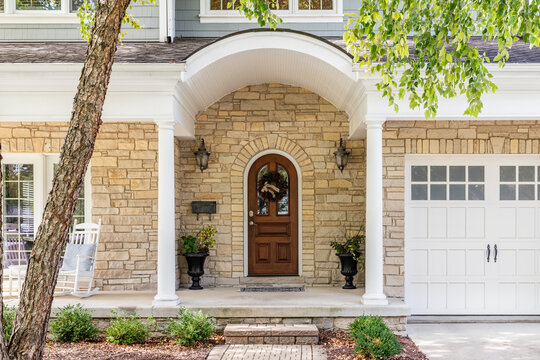 A front door detail with a rounded facade and front porch, a stone and blue siding, and a white garage door with windows.