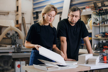 Young woman designer and man carpenter are discussing wooden furniture facade for kitchen project...