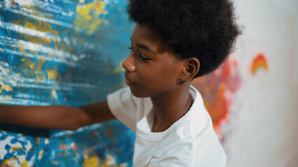 Side view of happy african boy painted the stained wall with colorful hand while wearing casual...