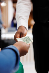 Close up of male African American waiter receiving tip from generous hotel guest. Tourist giving...