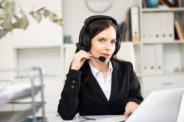 Female call center worker with headphones sitting at desk and looking at camera.