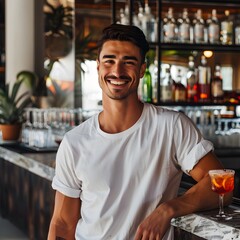 A man is smiling as he stands in front of a modern bar, wearing a plain white t-shirt.



