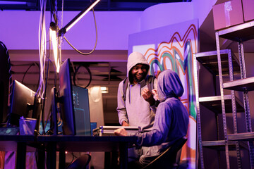Smiling hacker holding ssd with computer worm malicious software. Satisfied african american developer showing criminal disc with malware for password cracking in abandoned warehouse