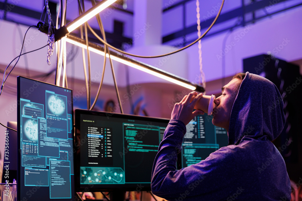 Poster hacker drinking coffee and attempting malware attack on web server. young man in hood doing criminal