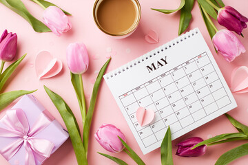 Honoring mothers: a day of tender sentiments and thankfulness. Top view shot of pink tulips, white gift box with, cup of coffee, May calendar surrounded by heart confetti on a pastel pink background