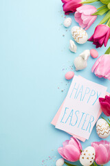 Easter elegance: a subtle celebration. Top view vertical shot of pink tulips, gentle "Happy Easter" note, patterned eggs, white bunny figures on a soft blue background with space for congratulations