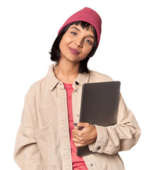 Cheerful young Hispanic student with laptop and beanie in studio