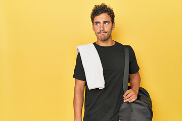 Young Latino athlete with backpack on yellow confused, feels doubtful and unsure. - obrazy, fototapety, plakaty