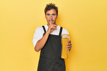 Young latino man cook with pasta jar on yellow keeping a secret or asking for silence. - obrazy, fototapety, plakaty