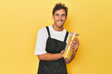 Young latino man cook with pasta jar on yellow laughing and having fun.